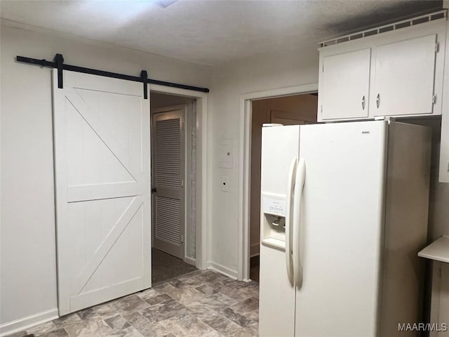 kitchen with a barn door, white fridge with ice dispenser, and white cabinets