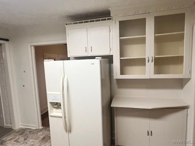 kitchen with white cabinetry, white refrigerator with ice dispenser, and a textured ceiling