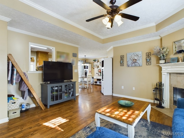 living room with ceiling fan, dark wood-type flooring, crown molding, a textured ceiling, and a tiled fireplace