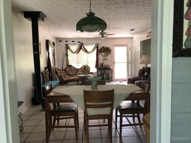 tiled dining room with a wood stove, ceiling fan, and a textured ceiling