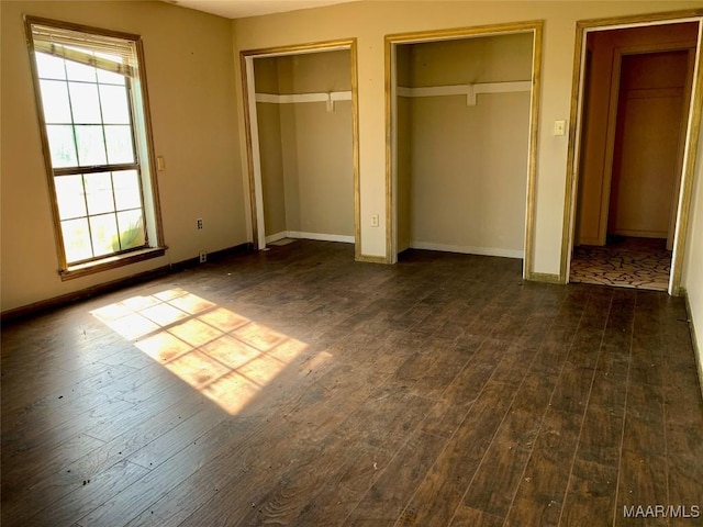 unfurnished bedroom with dark hardwood / wood-style flooring, multiple windows, and multiple closets