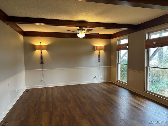 empty room featuring beamed ceiling, dark hardwood / wood-style floors, and a healthy amount of sunlight