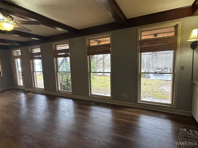 empty room with beamed ceiling, a wealth of natural light, dark wood-type flooring, and ceiling fan