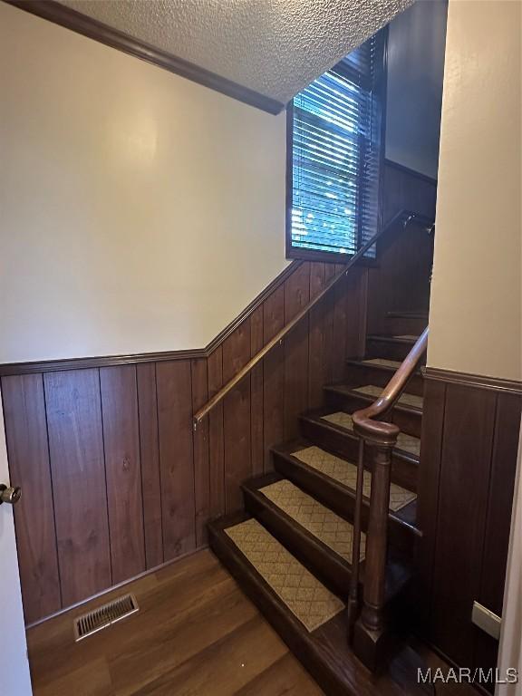 staircase featuring hardwood / wood-style floors, a textured ceiling, and wood walls