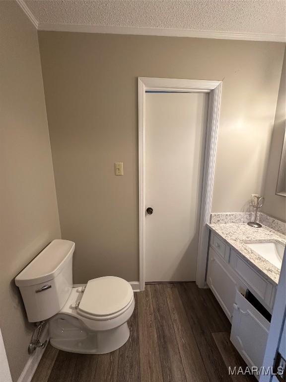 bathroom with crown molding, wood-type flooring, a textured ceiling, toilet, and vanity