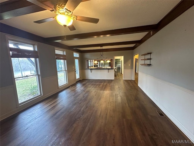 unfurnished living room with beam ceiling, dark wood-type flooring, and ceiling fan with notable chandelier