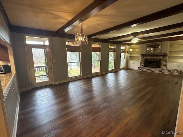 unfurnished living room with built in shelves, ceiling fan with notable chandelier, beam ceiling, a fireplace, and dark hardwood / wood-style floors