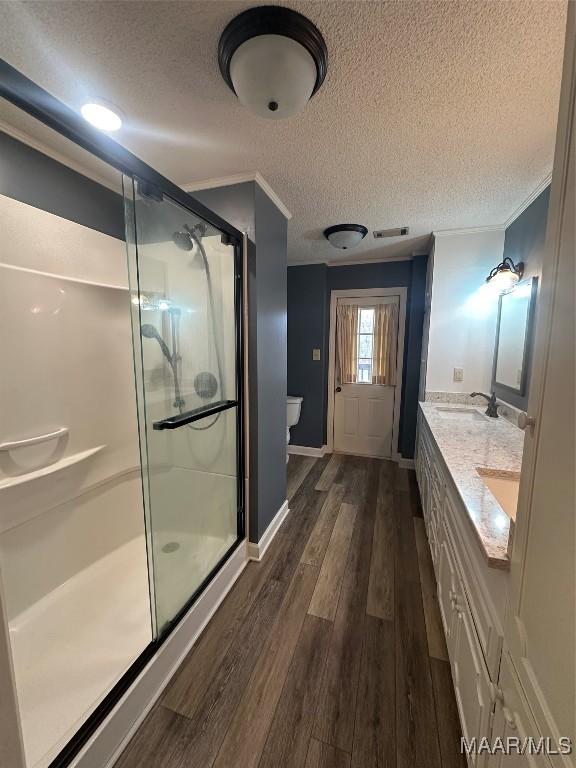 bathroom featuring vanity, wood-type flooring, toilet, a textured ceiling, and a shower with shower door