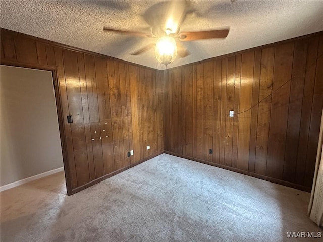 unfurnished bedroom featuring ceiling fan, light colored carpet, a textured ceiling, and wooden walls