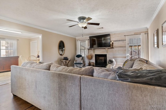 living room with ceiling fan, wood walls, ornamental molding, a textured ceiling, and dark hardwood / wood-style flooring