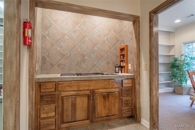 bar featuring built in shelves, light colored carpet, stainless steel gas stovetop, and crown molding