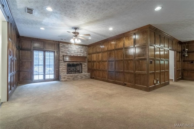 unfurnished living room featuring light carpet, a textured ceiling, ceiling fan, wooden walls, and a fireplace