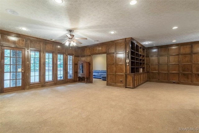 unfurnished living room featuring wooden walls, ceiling fan, a textured ceiling, and light carpet