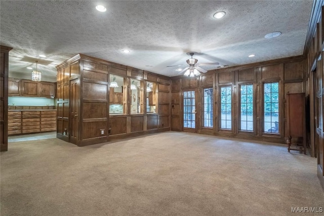 unfurnished living room featuring light carpet, a textured ceiling, ceiling fan, and wood walls