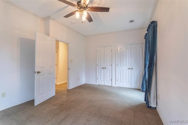 unfurnished bedroom featuring multiple closets, light colored carpet, ceiling fan, and crown molding