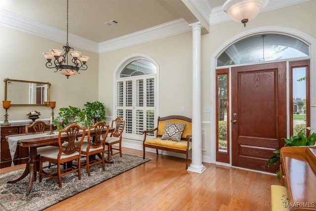 interior space with decorative columns, ornamental molding, light wood-type flooring, and an inviting chandelier