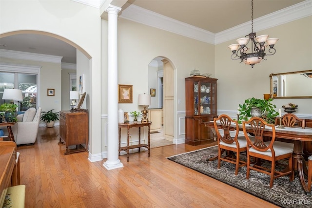 dining space featuring ornate columns, a chandelier, light wood-type flooring, and ornamental molding