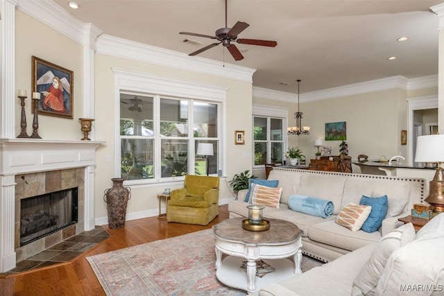 living room featuring a tiled fireplace, dark hardwood / wood-style flooring, ceiling fan with notable chandelier, and ornamental molding