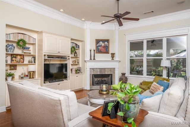 living room featuring ceiling fan, crown molding, dark wood-type flooring, and a tiled fireplace