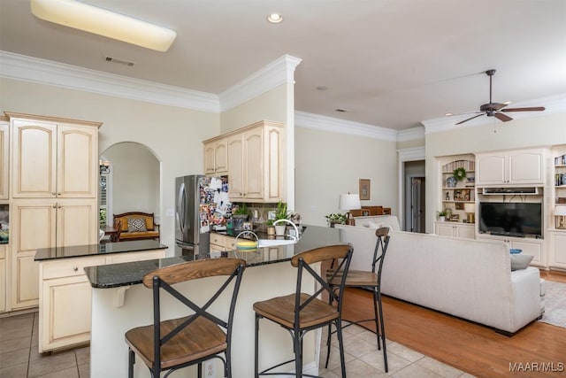 kitchen featuring stainless steel refrigerator, ceiling fan, cream cabinets, a kitchen bar, and light tile patterned floors