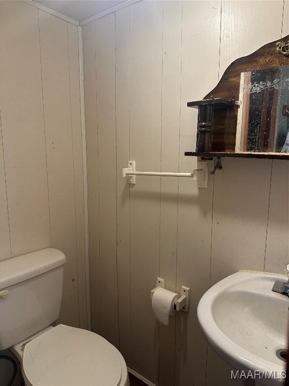 bathroom with toilet, wood walls, and sink