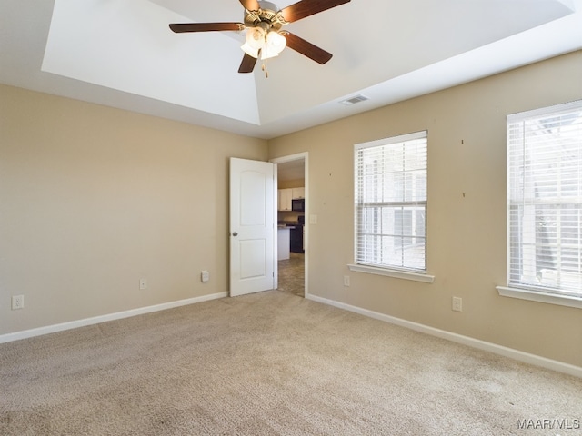 spare room with ceiling fan, light carpet, and a tray ceiling