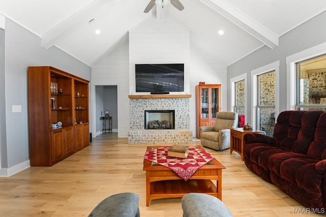 living room featuring vaulted ceiling with beams, ceiling fan, a large fireplace, and light wood-type flooring