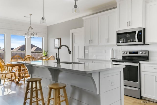 kitchen with a kitchen island with sink, white cabinets, sink, appliances with stainless steel finishes, and decorative light fixtures