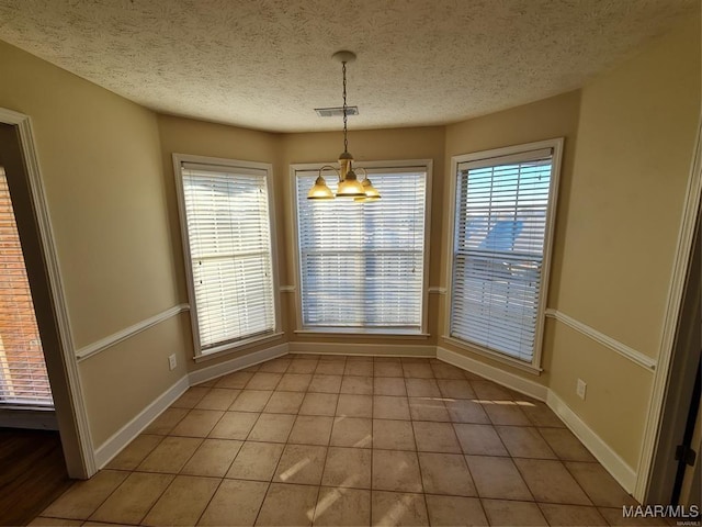 unfurnished dining area featuring light tile patterned floors, a textured ceiling, and an inviting chandelier