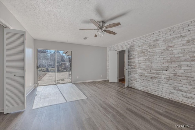 interior space featuring hardwood / wood-style flooring, ceiling fan, a textured ceiling, and brick wall