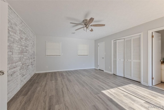 unfurnished bedroom featuring ensuite bath, light hardwood / wood-style flooring, ceiling fan, a textured ceiling, and brick wall