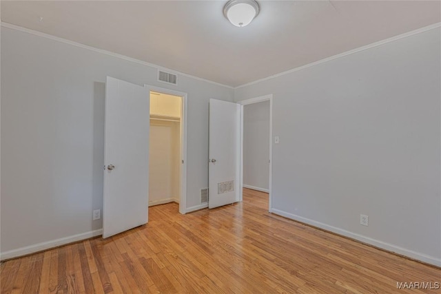 unfurnished bedroom featuring a walk in closet, crown molding, a closet, and light wood-type flooring