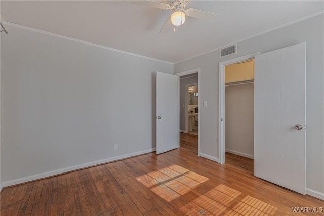 unfurnished bedroom with ceiling fan, crown molding, light hardwood / wood-style floors, a walk in closet, and a closet