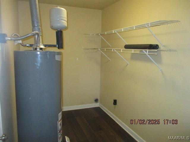 washroom with electric dryer hookup, dark wood-type flooring, and gas water heater