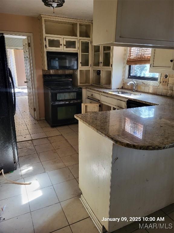 kitchen with light tile patterned flooring, a peninsula, a sink, dark stone counters, and black appliances