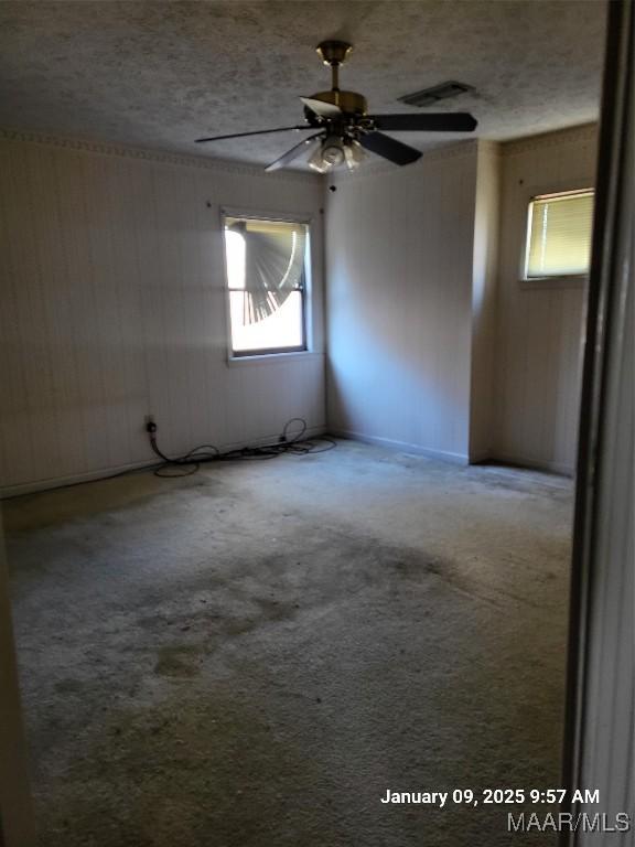 empty room featuring a textured ceiling, carpet flooring, visible vents, and a ceiling fan