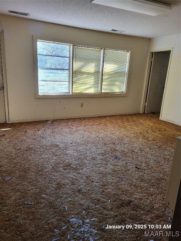 unfurnished room featuring carpet, visible vents, and a textured ceiling