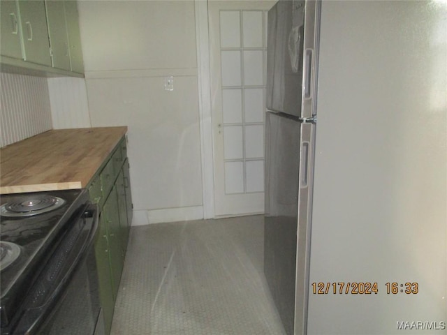 kitchen featuring stainless steel fridge, light tile patterned floors, butcher block countertops, black range with electric stovetop, and green cabinets