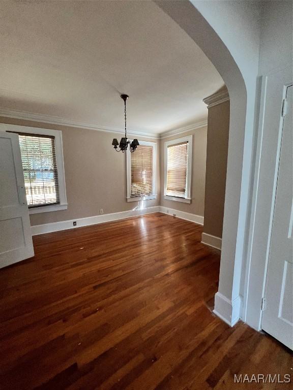 unfurnished dining area featuring crown molding, dark hardwood / wood-style floors, and an inviting chandelier