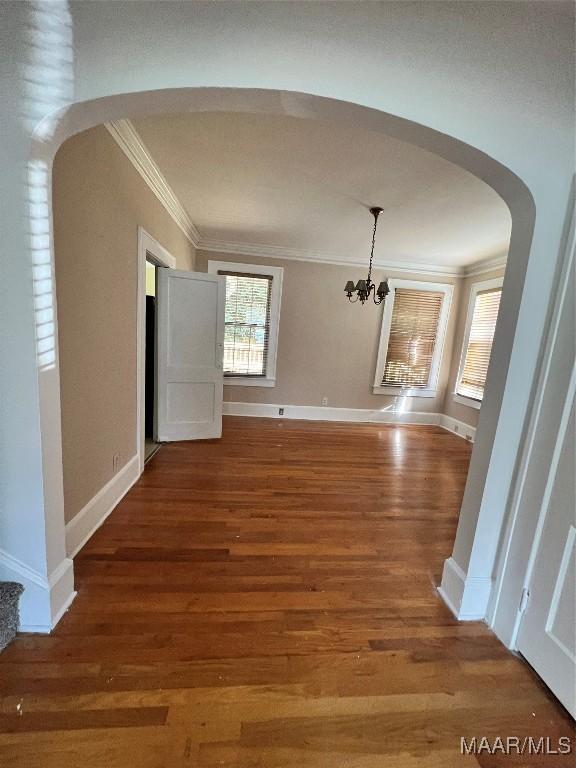 unfurnished dining area featuring ornamental molding, wood-type flooring, and an inviting chandelier