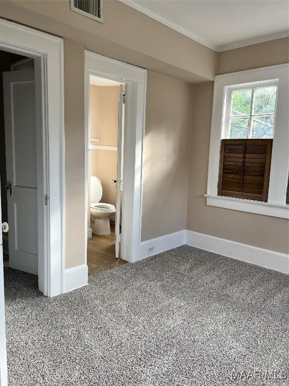 unfurnished bedroom featuring ensuite bath, carpet floors, and ornamental molding