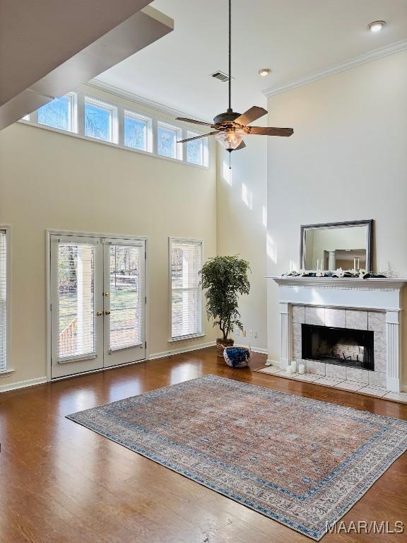 unfurnished living room with french doors, dark hardwood / wood-style flooring, ornamental molding, ceiling fan, and a fireplace