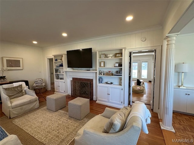 living room with a brick fireplace, built in features, parquet floors, and ornate columns