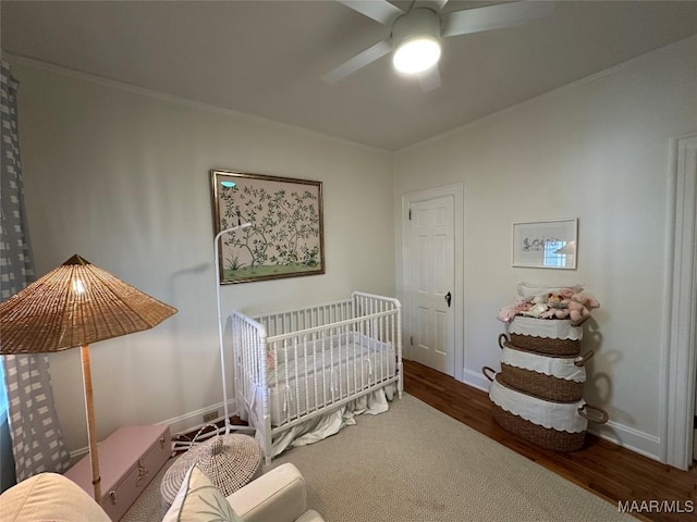 bedroom featuring ceiling fan, dark wood-type flooring, and a crib