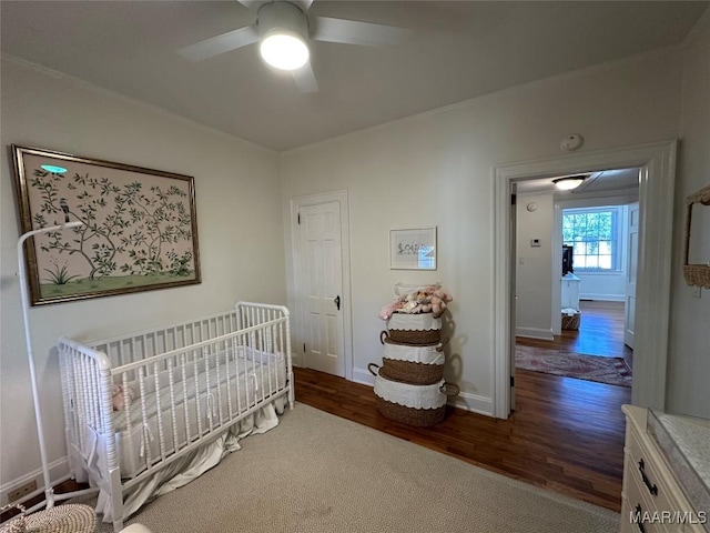 bedroom with dark hardwood / wood-style flooring, a nursery area, and ceiling fan