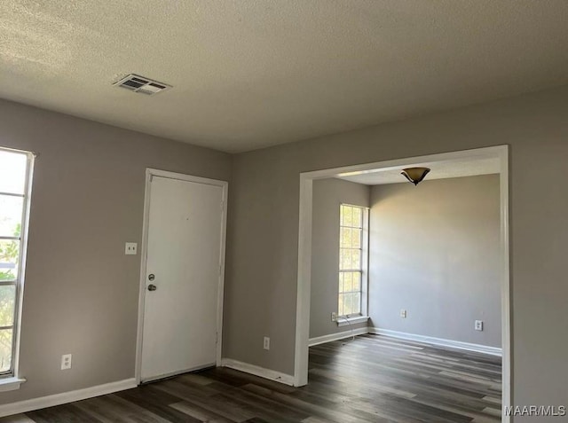 empty room featuring a textured ceiling, dark hardwood / wood-style floors, and a healthy amount of sunlight