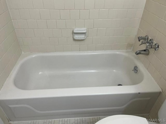 bathroom with a tub to relax in and toilet