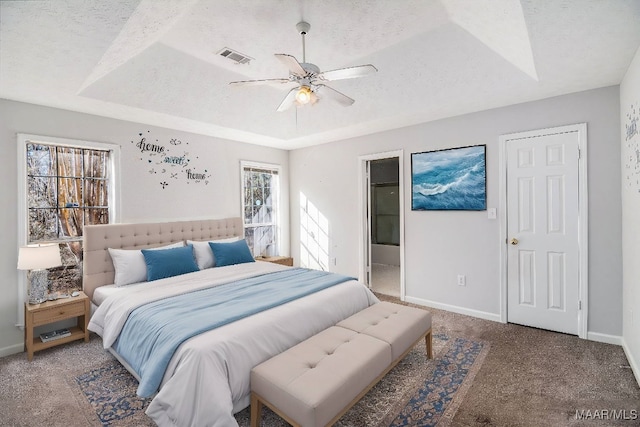 carpeted bedroom with a tray ceiling, ensuite bath, ceiling fan, and a textured ceiling