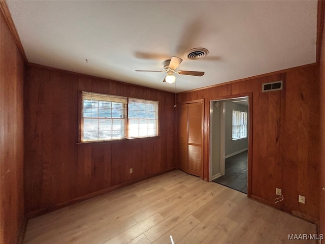 unfurnished bedroom featuring ceiling fan, a closet, wood walls, and light hardwood / wood-style flooring