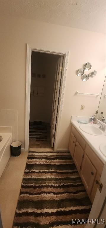 bathroom with a textured ceiling, vanity, and a tub to relax in